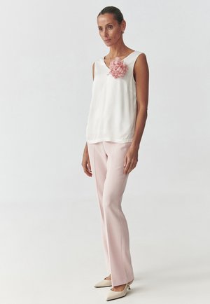 White sleeveless top with a pink fabric flower detail, paired with light pink tailored pants and beige heels, on a neutral background.