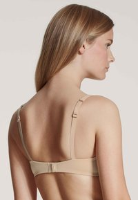 Beige bra with adjustable straps, smooth fabric, hook-and-eye closure at the back, and minimalistic design.
