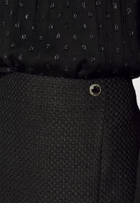 Top de tela negra texturizada con manchas brillantes combinado con una falda negra texturizada a juego que presenta un detalle de botón en tono dorado.