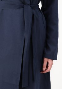 Navy blue cotton wrap dress with a tie belt, featuring a smooth texture and long sleeves. Includes side pockets and a straight cut.