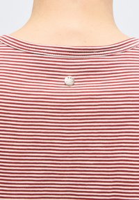 Λαιμός και πάνω μέρος της πλάτης ενός ατόμου που φοράει κόκκινη και λευκή οριζόντια ριγέ μπλούζα με μικρό στρογγυλό ασημένιο κουμπί στο κέντρο του γιακά.