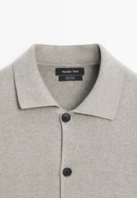 Lichtgrijze katoenen polo met een kraag en drie zwarte knopen aan de voorkant, gemaakt van een zachte, gestructureerde gebreide stof.