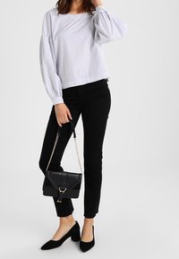 Blouse blanche à rayures avec manches bouffantes, jean skinny noir, ballerines noires à bout pointu, et petit sac bandoulière noir avec des accents dorés.