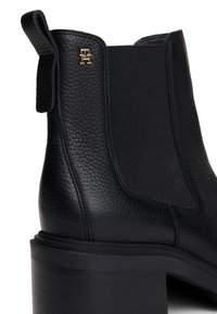 Bottine en cuir noir texturé avec panneau latéral élastique, languette de tirage, talon bloc et petit logo doré près du bord supérieur.