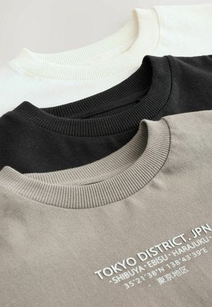 Tre crewneck sweatshirts i vitt, svart och grått, med ribbad krage och grafisk text på den grå tröjan, i mjukt bomullsmaterial.