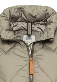 Lys beige quiltet jakke med høj krave. Har en lynlås med en orange trækflig og en label syet indeni. Indersiden har en glat tekstur.