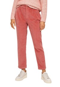 Puserot vaaleanpunaisessa värissä, jossa on röpelöinen pinta, korkealla vyötäröllä ja kapeilla lahkeilla, yhdistetty valkoisiin tenniskenkiin.