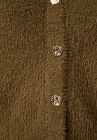 Bruine fuzzy cardigan met metalen, onregelmatig gevormde knopen. De textuur is zacht en fluffy, wat het knusse uiterlijk versterkt.