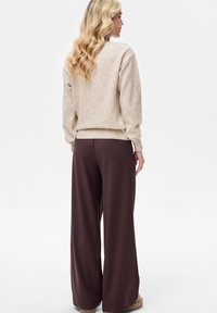 Beżowy dziergany sweter z wzorem w diamenty, zestawiony z szerokimi brązowymi spodniami. Sweter ma ściągacze na mankietach i dole.