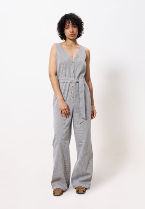 Combinaison rayée gris clair avec un décolleté en V, boutons sur le devant, une ceinture nouée à la taille et une coupe évasée. Portée avec des sandales à lanières marron.