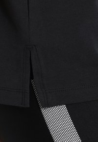 Černý lem oděvu s bočním rozparkem, pod kterým se objevují černé legíny s bílým tečkovaným pruhem.