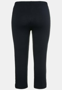 Černé elastické capri kalhoty s elastickým pasem, mají hladký povrch a rovný střih, končí těsně pod kolenem.