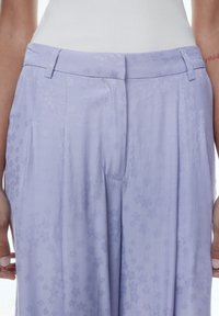 Lila broek met een gestructureerd bloemenpatroon, voorzien van een vlakke voorkant, zijzakken en een getailleerde pasvorm. Gladde stofafwerking.