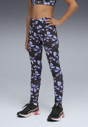 Leggings noirs à motif floral bleu et violet, en matériau extensible, assortis à des chaussures de sport noires et roses.