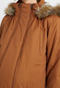 Brown insulated parka jacket featuring a faux fur hood, front zip closure, and side pockets, made from a smooth, textured material.