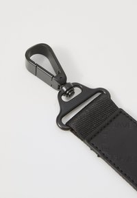 Czarny materiałowy pasek z gładką skórzaną zakładką i matowym czarnym karabinkiem metalowym; trwały, teksturowany i praktyczny design.