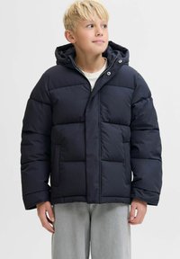 Marineblå pufjakke med hætte, der har et quiltet design, frontlynlås og knaplukninger. Materialet er glat med en mat finish.