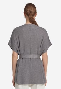 Grå metallisk topp med bälte, korta ärmar och en lös passform. Har en texturerad tyg och en lagerdesign bak.