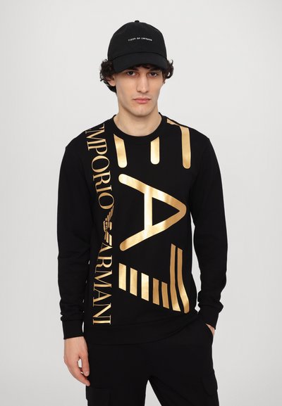 Sweatshirt noir avec de grandes lettres et graphiques dorés, doté d'un col rond et de manches longues. Tissu lisse avec un design moderne.