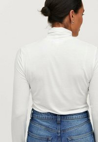 Hvid langærmet turtleneck top med en glat tekstur, parret med højtaljede blå jeans med baglommer og en tætsiddende silhuet.