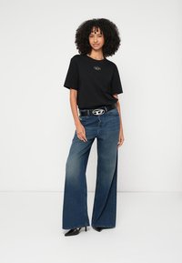 Tricou negru cu un logo mic, asortat cu blugi albaștri cu picioare largi, ținuți cu o curea neagră cu o cataramă argintie, și pantofi cu toc negri.