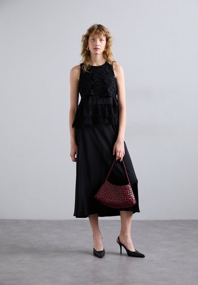 Must mustriga kleit lillelise pitsipealse ja siledast kangast seelikuga, koos punase pruuni punutud käekotiga ja mustade kõrge kontsaga kingadega.