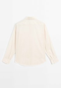 Lys beige langærmet skjorte med klassisk krave, knapmanchetter og afrundet kant. Glat tekstur med et subtilt vævet mønster.