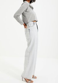 Grauer Cropped-Top mit langen Ärmeln, kombiniert mit hellgrauen, weit geschnittenen Jeans und grauen, hohen Sandalen, die eine hohe Taille und einen Knopfverschluss haben.