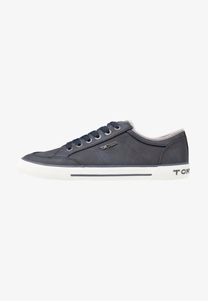 Zapatilla deportiva baja de color azul oscuro con suela de goma blanca, cordones azules y el logo "Tom Tailor" en el lateral y el talón.