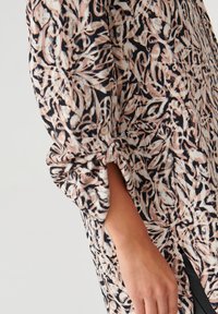Blusa con fantasia floreale in nero, bianco e rosa chiaro; tessuto leggero; maniche arrotolate; spacchi laterali per maggiore movimento.