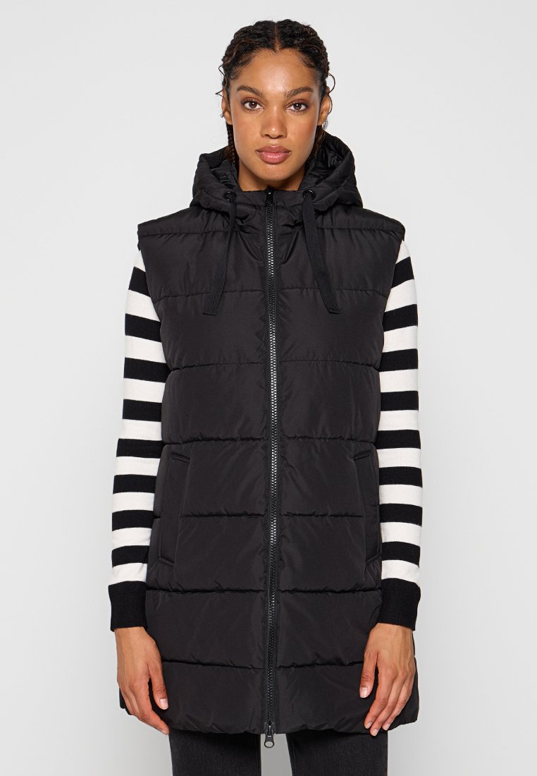 Gilet imbottito nero con cappuccio staccabile, dotato di una zip frontale, due tasche e una texture trapuntata abbinato a una camicia a maniche lunghe a righe.