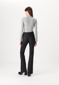 Sivi rebrasti crop top s dugim rukavima i otvorenim stranama, uparen s crnim hlačama visokog struka sa širokim nogavicama. Glatka tekstura i prilagođeni dizajn.