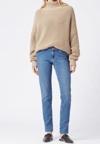 Beige knitted turtleneck sweater with ribbed texture, paired with blue slim-fit jeans and black flat shoes.