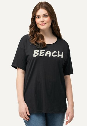 T-shirt noir en tissu doux, arborant un texte « BEACH » en blanc audacieux sur le devant. Coupe ample avec des manches courtes et un col rond.