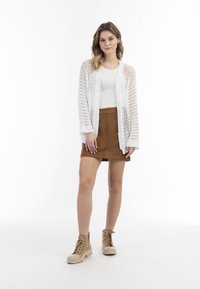 Witte gebreide cardigan met open weving, beige tanktop, bruine rok en tan kleurige veterschoenen. Eenvoudig ontwerp met een casual, gelaagd uiterlijk.