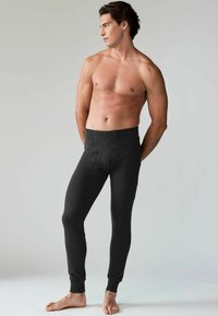 Leggings noirs côtelés en tissu extensible, présentant une coupe ajustée, une taille élastique et des poignets fuselés. Aucun motif ni logo visible.