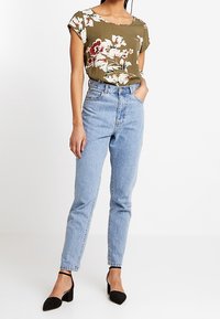 Oliven grøn blomsterprint top med korte oprullede ærmer, parret med lyseblå højtaljede denimjeans og sorte hæle.