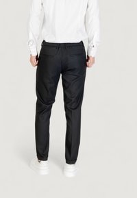 Pantalones negros ajustados con un corte relajado, con una parte delantera plana, cintura elástica y dos bolsillos traseros. Llevados con zapatillas blancas.