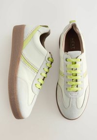 White leather sneakers with lime green accents and laces, featuring a suede toe cap and textured brown rubber sole.