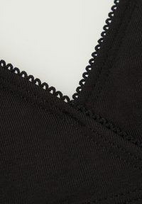 Czarny stanik sportowy z ribbowanej tkaniny, o dekolcie w kształcie litery V oraz falbaniastym wykończeniu z koronki wzdłuż dekoltu. Miękka tekstura i elastyczny materiał.
