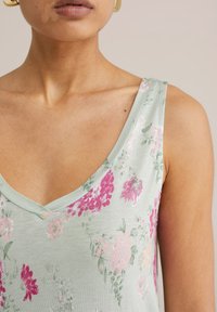 Svijetlozeleni cvjetni top bez rukava s V-izrezom, ukrašen ružičastim i ljubičastim cvjetovima. Mekana tkanina i dizajn bez rukava.