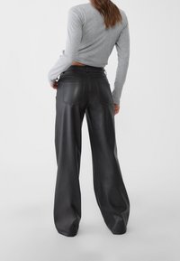 Pantalones de piel negra de pierna ancha con bolsillos traseros, combinados con una camiseta ajustada de manga larga en gris claro. Textura suave y ajuste a medida.