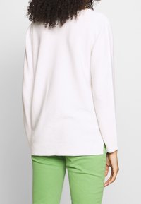 Helles rosa Sweatshirt aus geripptem Material, mit langen Ärmeln und lockerer Passform. Kombiniert mit grünen.Hosen, die ein entspanntes Design zeigen.