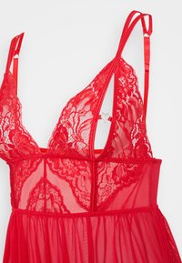 Nuisette en dentelle rouge avec un tissu transparent, des motifs floraux délicats, des bretelles en satin ajustables et un accent en forme de cœur au dos.