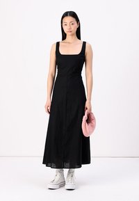 Rochie neagră, fără mâneci, cu decolteu pătrat, realizată dintr-un material ușor, care ajunge până la jumătatea gambei. Asortată cu o geantă roz și adidași albi.