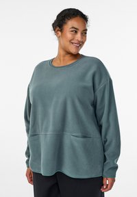 Svetlo modrozelená mikina z fleecu s voľným strihom, okrúhlym výstrihom, dlhými rukávmi a vreckom v páse. Mäkká textúra s zakriveným okrajom.