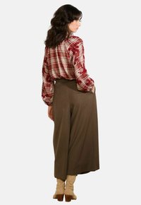 Rood geruit overhemd met bloemenborduring op de mouwen, gecombineerd met hoge, wijde bruine broeken en beige enkellaarsjes.