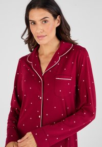Bordeaux pyjamaset met een knoopsluiting, witte sterrenpatronen, een borstzak en contrasterende piping op de kraag en mouwen.