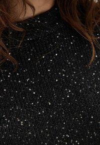 Czarny sweter wykonany na drutach o prążkowanej fakturze, ozdobiony rozsianymi srebrnymi cekinami. Wysoki dekolt z gładkim wykończeniem.