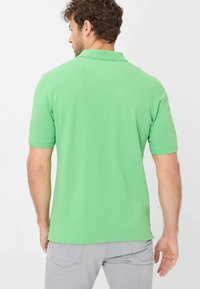 Polo verde con maniche corte, slim fit e texture morbida. Presenta un colletto classico e dettagli di cucitura sottili.